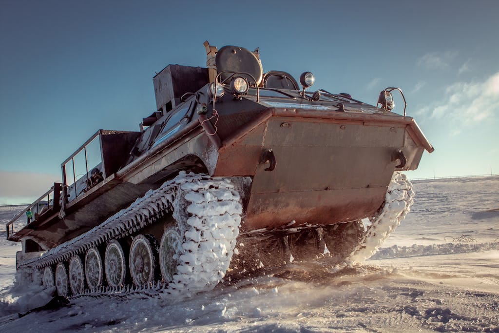 A heavy military vehicle navigating through a snowy landscape under bright skies.