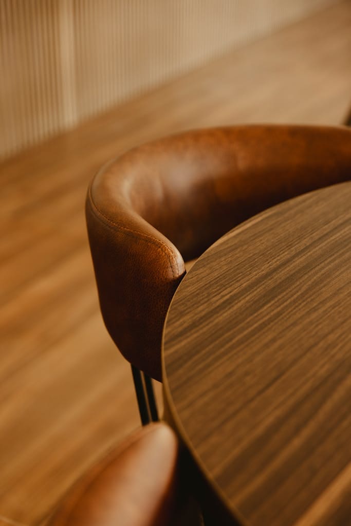 A stylish brown leather chair next to a smooth wooden table in a warm indoor setting.